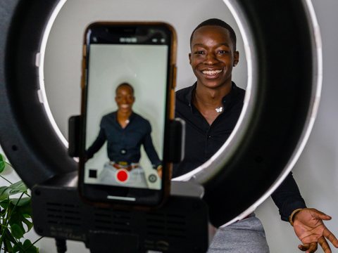 Profissional sorridente gravando um vídeo com o celular em um aro de luz