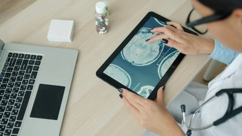 Mãos segurando um tablet com uma imagem de ressonância, laptop ao lado