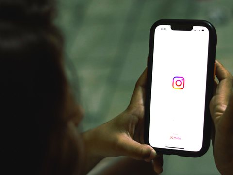 Mão segurando um celular com a tela de abertura do Instagram